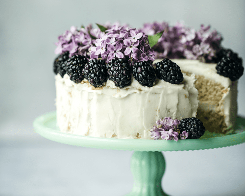 Blackberry and flower topped cake mounted on a cake stand